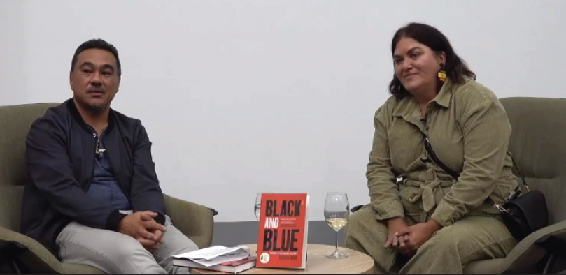 Two people sitting on armchairs having a discussion with a side table with books and wine